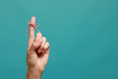 Photo of Woman showing index finger with tied bow as reminder on light blue background, closeup. Space for text