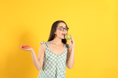 Concept of choice. Woman eating apple and holding doughnut on yellow background