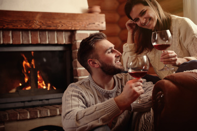 Lovely couple with glasses of wine near fireplace indoors. Winter vacation