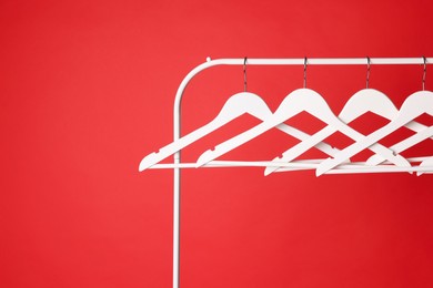 White clothes hangers on metal rack against red background