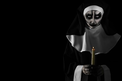 Scary devilish nun with burning candle on black background, space for text. Halloween party look