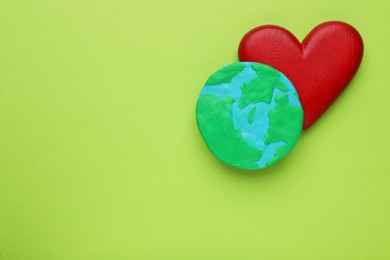 Model of planet and red heart on green background, flat lay with space for text. Earth Day