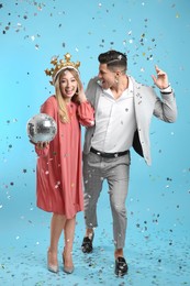 Happy couple with disco ball and confetti on light blue background