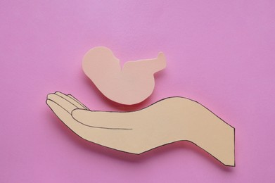 Photo of Woman`s health. Hand with newborn paper figure on pale pink background, flat lay