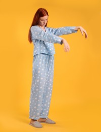 Young woman wearing pajamas and slippers in sleepwalking state on yellow background