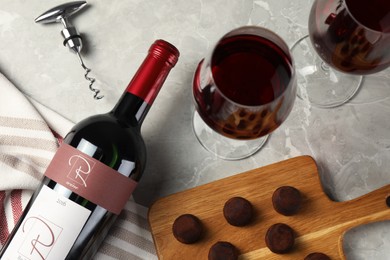 Glasses and bottle of red wine with chocolate on light marble table, flat lay