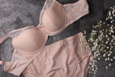 Elegant beige plus size women's underwear and gypsophila flowers on grey background, flat lay