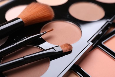 Photo of Colorful contouring palettes with brushes, closeup. Professional cosmetic product