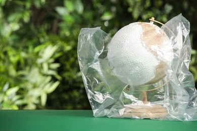 Photo of Globe in plastic bag on table against green leaves, space for text. Environmental conservation