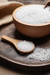 Bowl and spoon with natural sea salt on wooden table, closeup