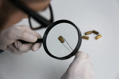 Detective exploring bullet shell with magnifying glass, closeup