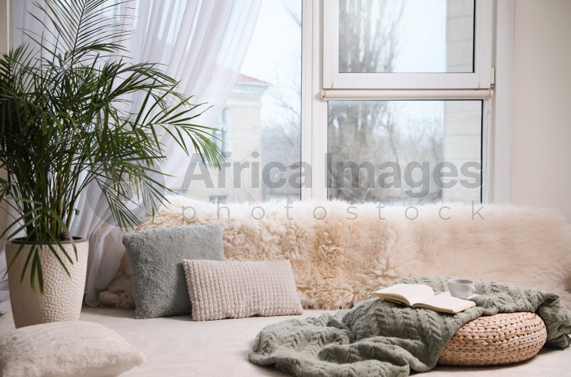 Photo of Comfortable lounge area with faux fur and pillows near window in room