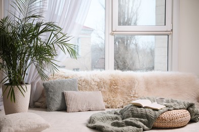 Comfortable lounge area with faux fur and pillows near window in room