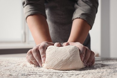 Photo of Man kneading dough at table in kitchen, closeup