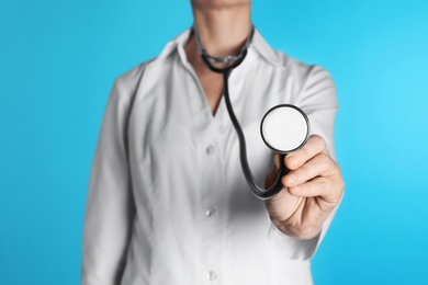 Female doctor holding stethoscope on color background, closeup. Medical object