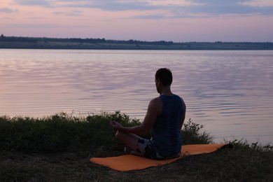 Man meditating near river in twilight, back view