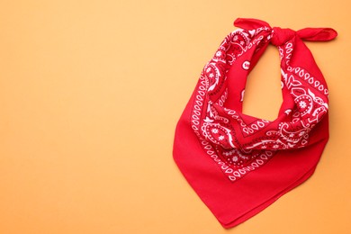Tied red bandana with paisley pattern on orange background, top view. Space for text