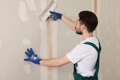 Photo of Worker in uniform plastering wall with putty knife indoors