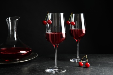 Delicious cherry wine with ripe juicy berries on grey table against black background