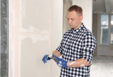 Worker with putty knives and plaster near wall indoors. Home renovation