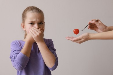 Cute little girl covering mouth and refusing to eat tomato on grey background