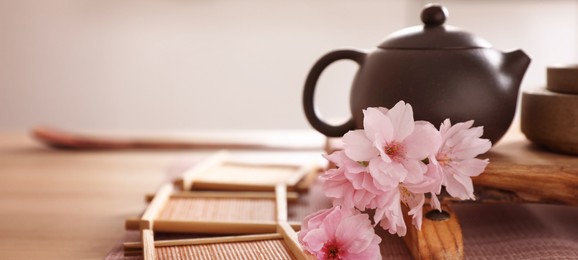 Pot, sakura flowers and bamboo coasters for traditional tea ceremony on table. Banner design