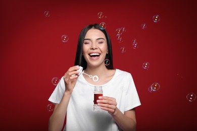 Photo of Young woman having fun with soap bubbles on red background