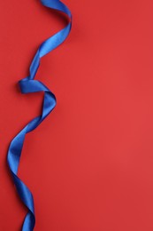 Photo of Beautiful blue ribbon on red background, top view. Space for text