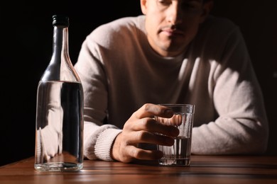 Addicted man with alcoholic drink at wooden table against black background, closeup