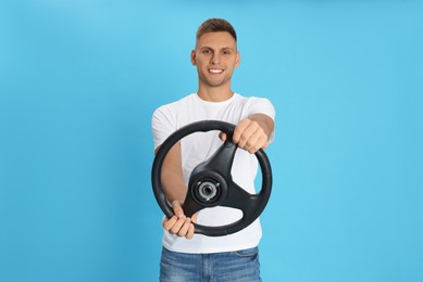 Happy man with steering wheel on light blue background