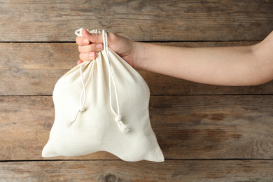 Woman holding full cotton eco bag on wooden background, closeup