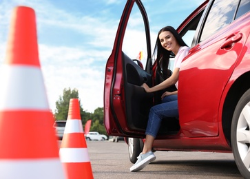 Young woman in car near traffic cones outdoors. Driving school exam