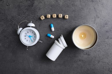 Word Sleep made of wooden cubes near alarm clock, candle and pills on grey background, flat lay. Insomnia treatment