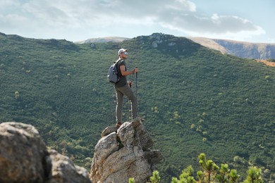 Photo of Hiker with trekking poles standing on rocky peak in mountains
