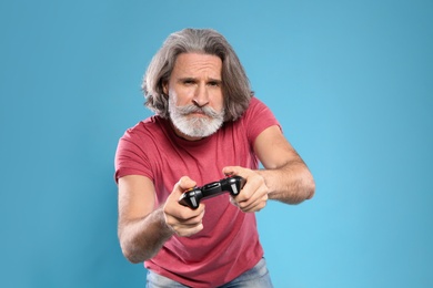 Emotional mature man playing video games with controller on color background