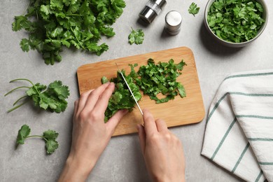 Woman cutting fresh green cilantro at light grey table, top view