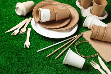 Photo of Eco disposable tableware on green artificial grass. Space for text