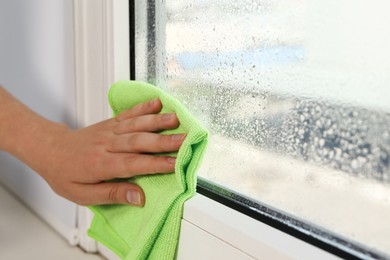 Woman wiping window glass with drops of condensate indoors, closeup