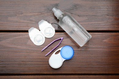 Packages with contact lenses, case, tweezers and drops on wooden table, flat lay