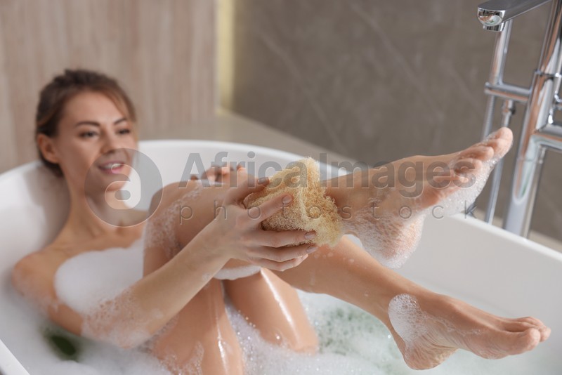 Beautiful woman with loofah taking bath indoors, focus on legs