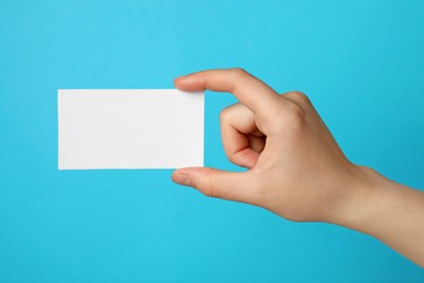 Photo of Woman holding blank gift card on light blue background, closeup
