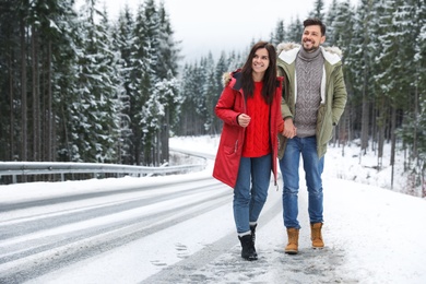 Photo of Couple walking near snowy forest, space for text. Winter vacation
