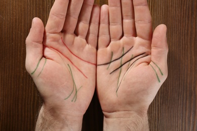 Man showing palms with drawn lines on wooden background, top view. Chiromancy and foretelling