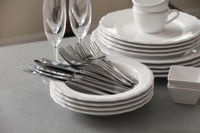 Set of clean dishware, cutlery and champagne glasses on grey table 