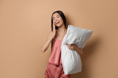 Beautiful Asian woman with pillow on beige background. Bedtime