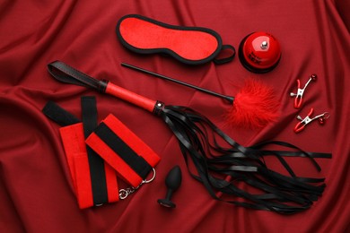 Photo of Sex toys and accessories on red fabric, flat lay