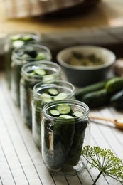 Photo of Set of glass jars with fresh cucumbers prepared for canning on table