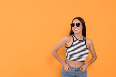 Attractive happy woman in fashionable sunglasses against orange background. Space for text