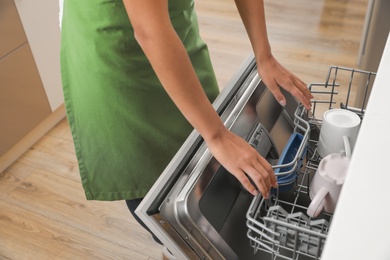 Woman opening dishwasher in kitchen, closeup. Cleaning chores