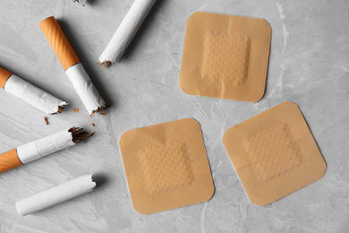 Photo of Nicotine patches and broken cigarettes on grey table, flat lay